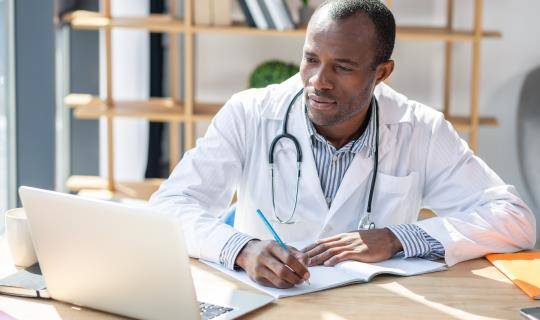 Doctor looks at laptop and takes notes